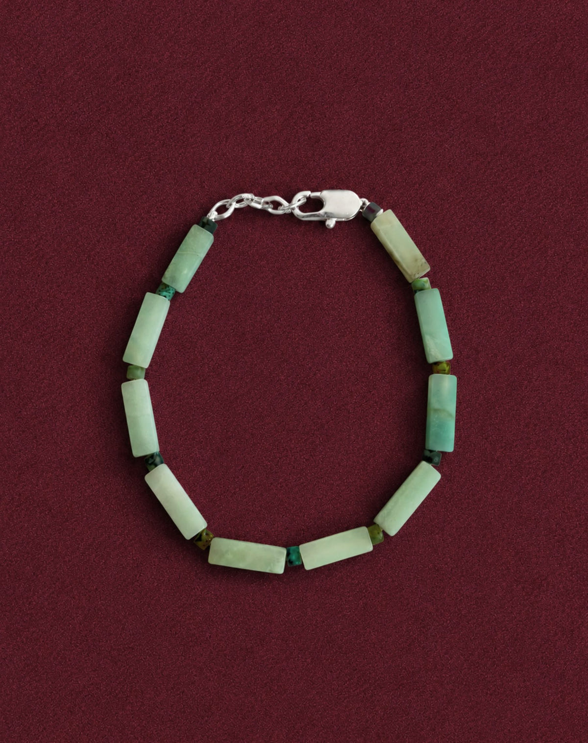Pale green tube beads with dark green accents and a silver clasp, on burgundy