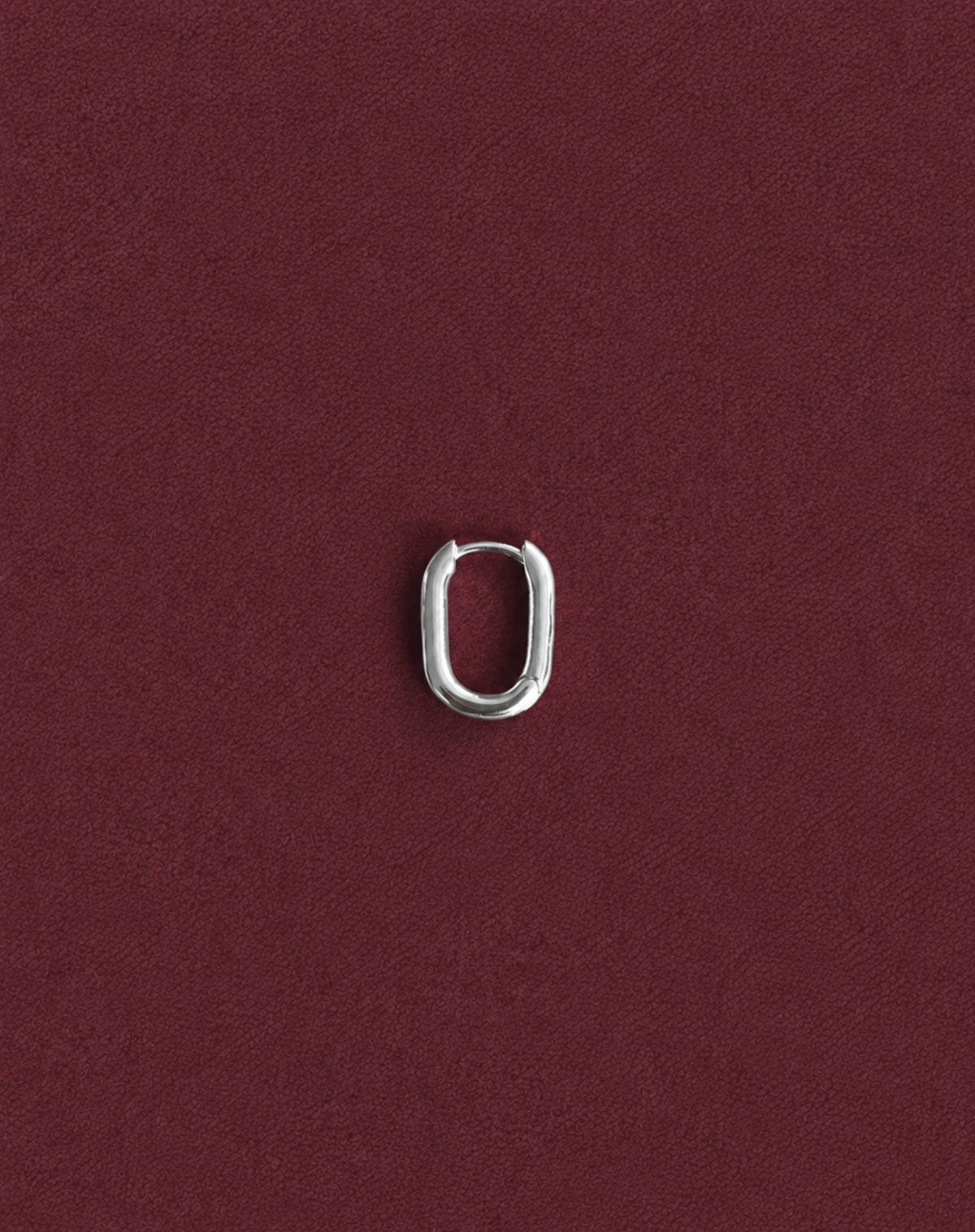Single silver oval hoop, on burgundy fabric