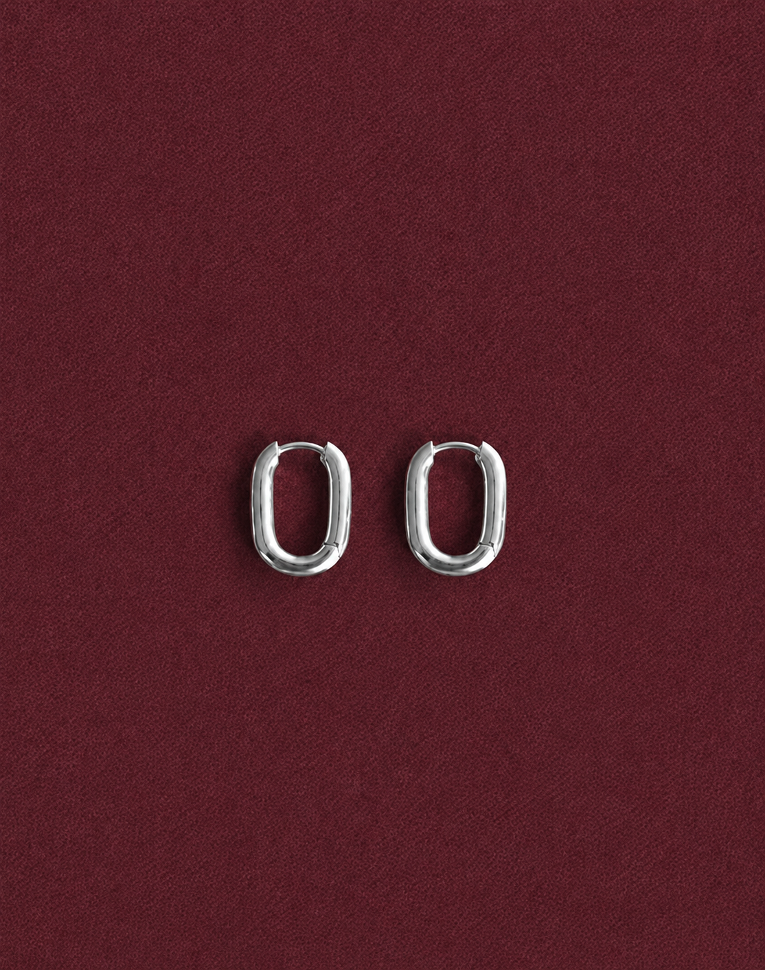 The pair of silver hoops side by side on the same burgundy fabric