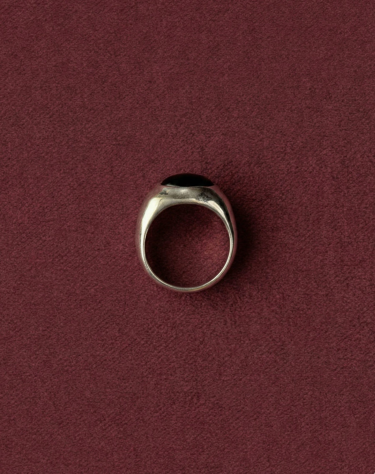 Domed silver setting with a black oval cabochon, upright on burgundy velvet