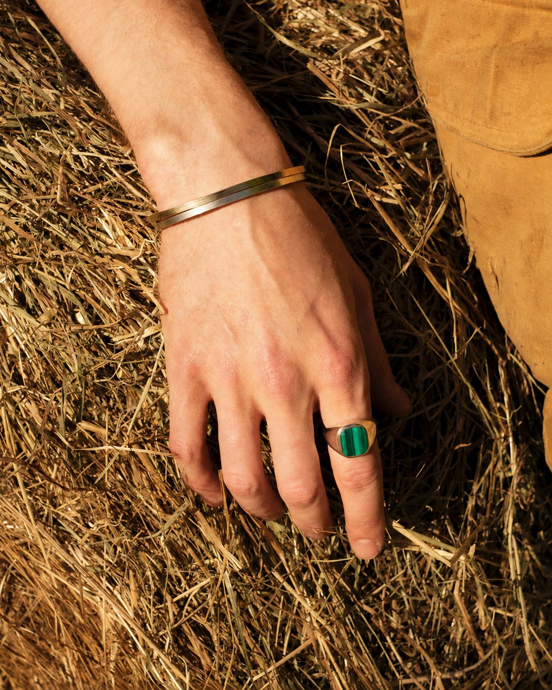 Rectangular green stone in gold on the ring finger, gold bangle, hand on straw
