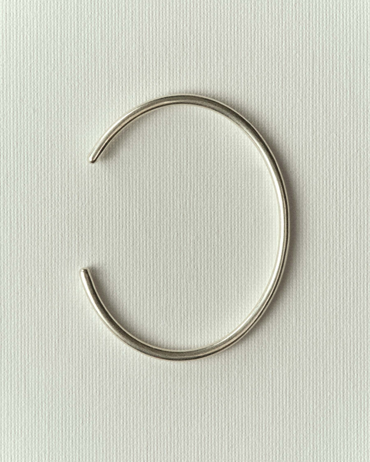 Open cuff in round silver wire, laid flat on textured off-white paper