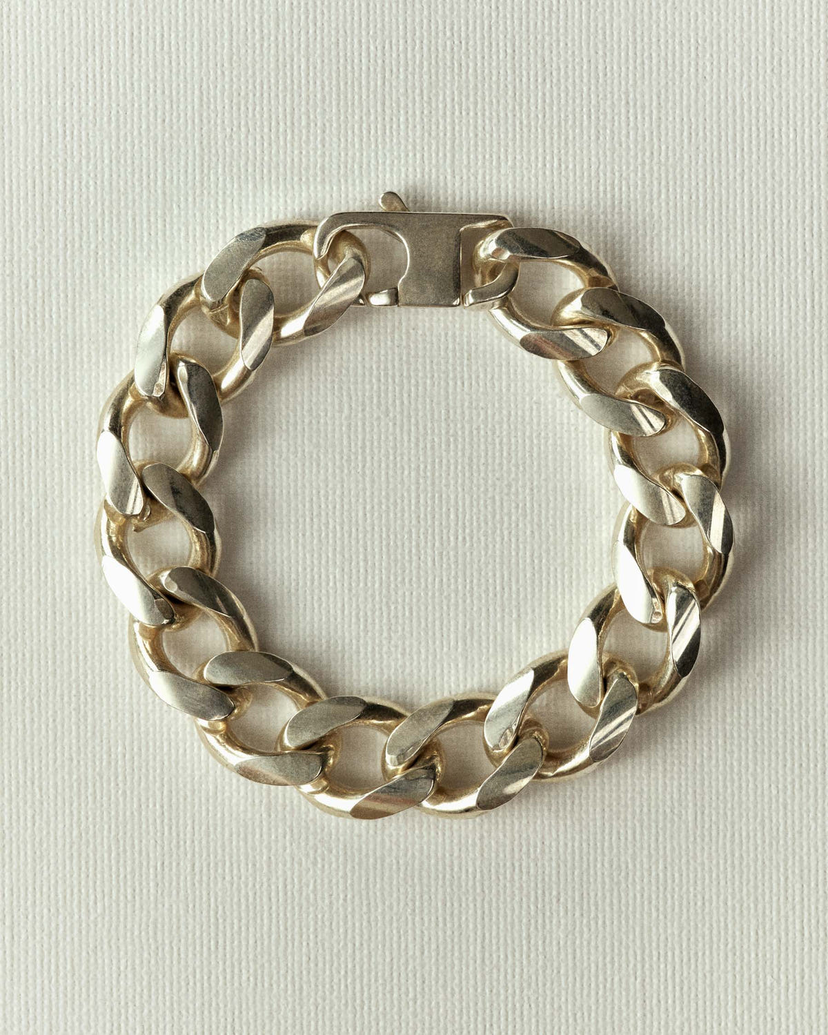 Heavy silver curb links with a plaque clasp, flat on off-white paper