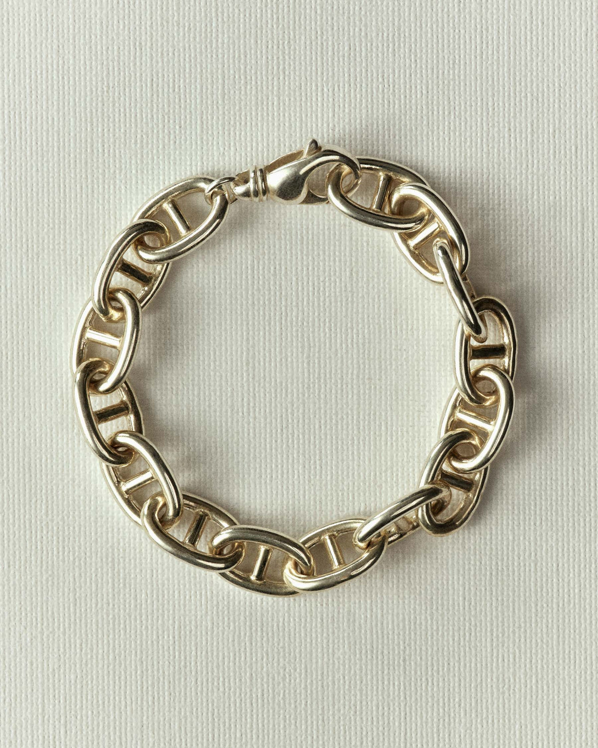 Chunky gold anchor links with a lobster clasp, coiled on cream paper