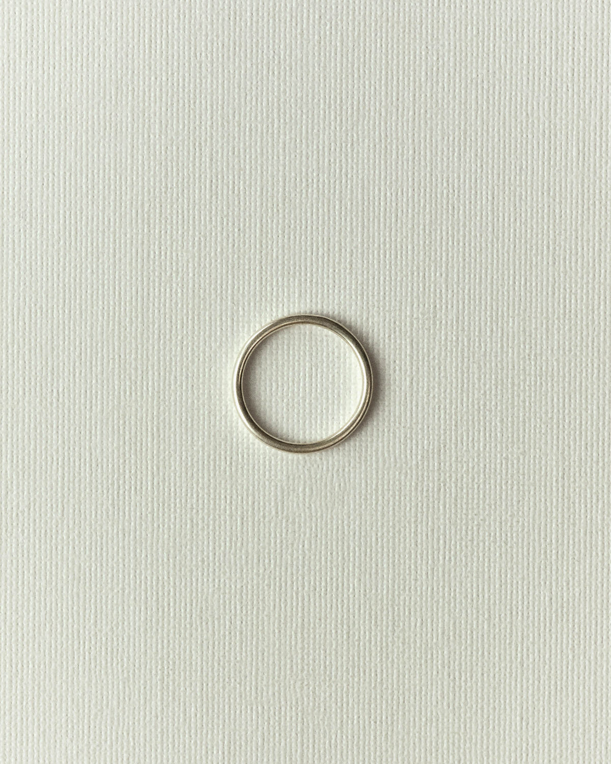 Thin silver band lying flat on textured off-white paper