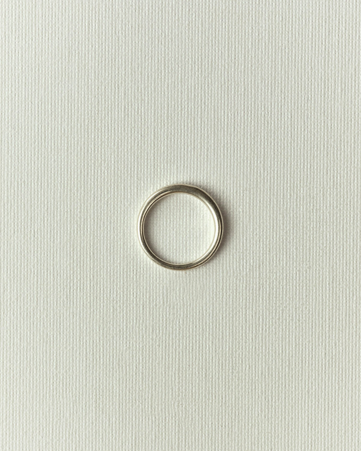 Fine smooth silver band, standing on textured off-white paper