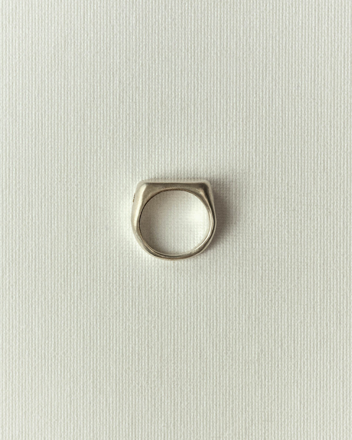 Matte silver band with a wide irregular top, standing upright on off-white paper