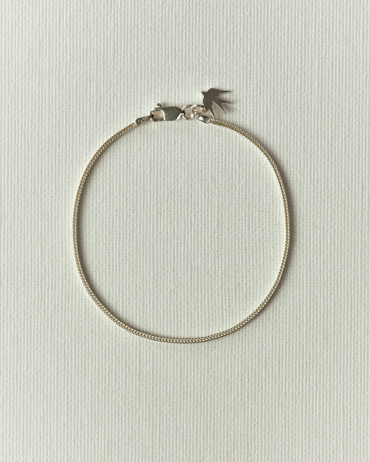 Fine silver chain laid in a circle, lobster clasp and small bird charm