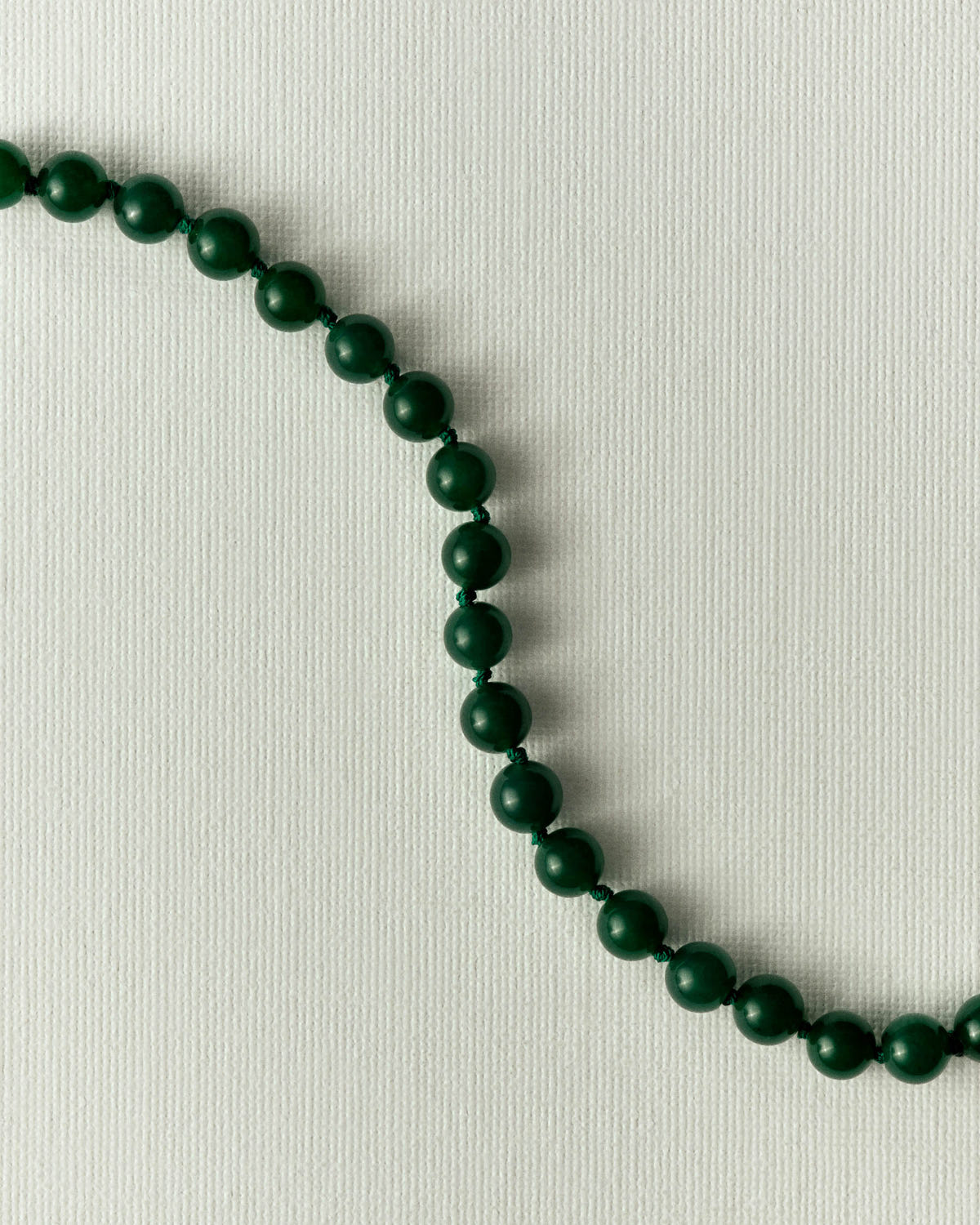 Close-up of matte dark green beads, knotted and running diagonally across a cream ground