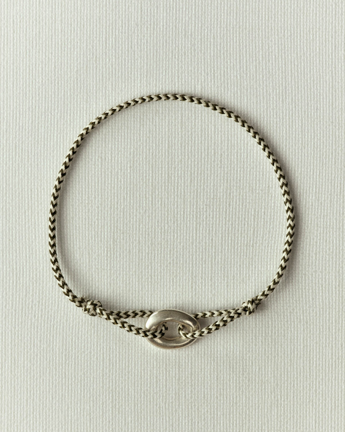 Khaki and black braided cord with a silver oval link, on textured paper