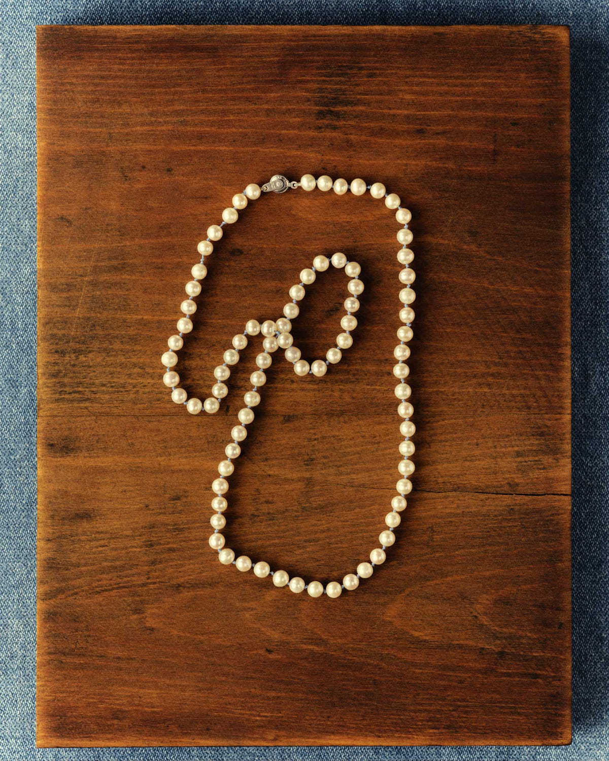 Long strand of cream pearls coiled on a wooden board over denim