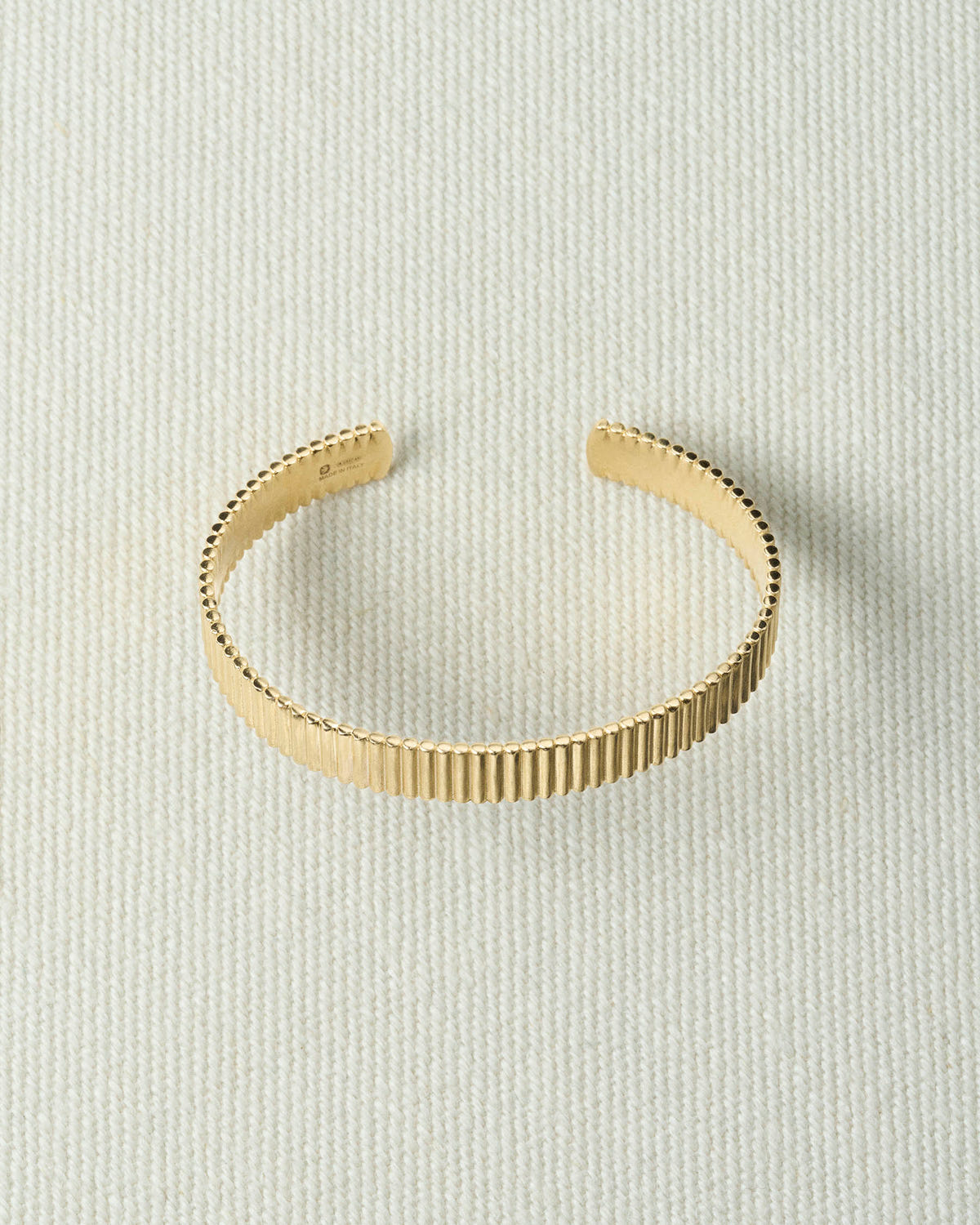Wide ribbed gold cuff, open at the back, lying flat on textured ecru canvas
