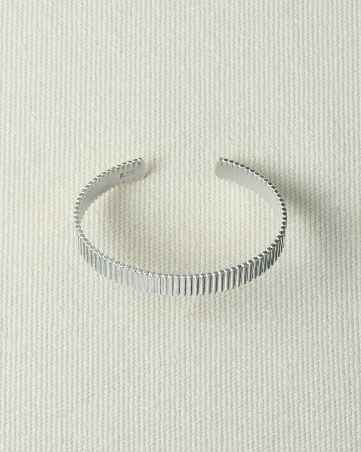 Wide ribbed silver cuff, open at the back, lying flat on textured ecru canvas