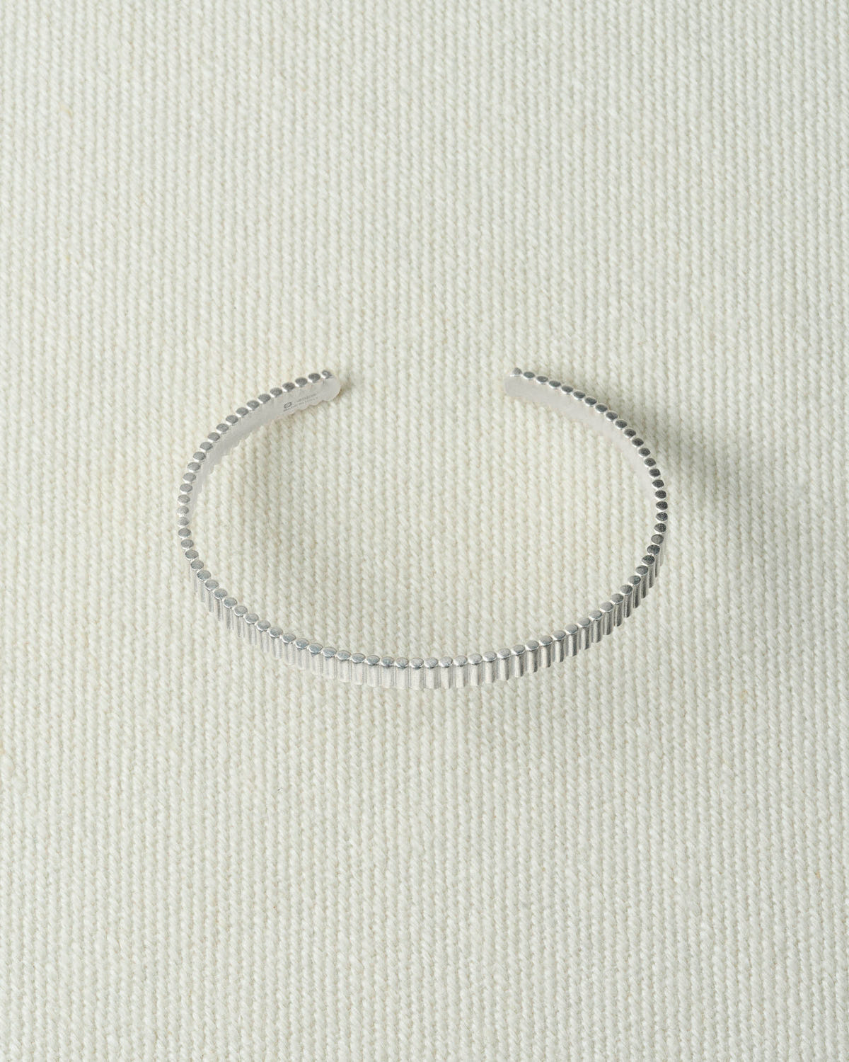 Thin ribbed silver cuff, open at the back, lying flat on textured ecru canvas