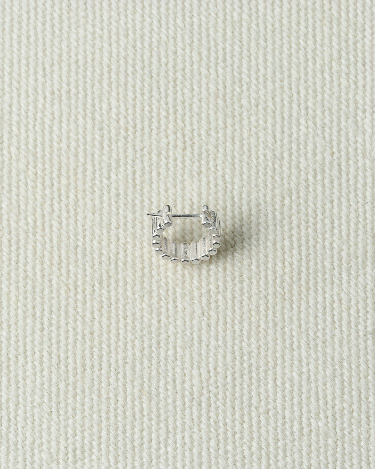 Single silver hoop, ribbed with beaded edges, on textured ecru canvas