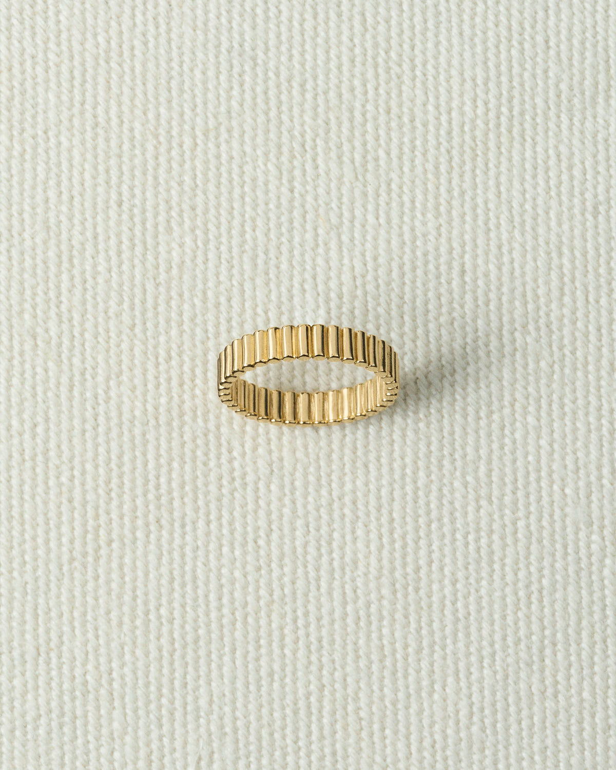 Narrow gold ribbed band lying flat on textured ecru canvas