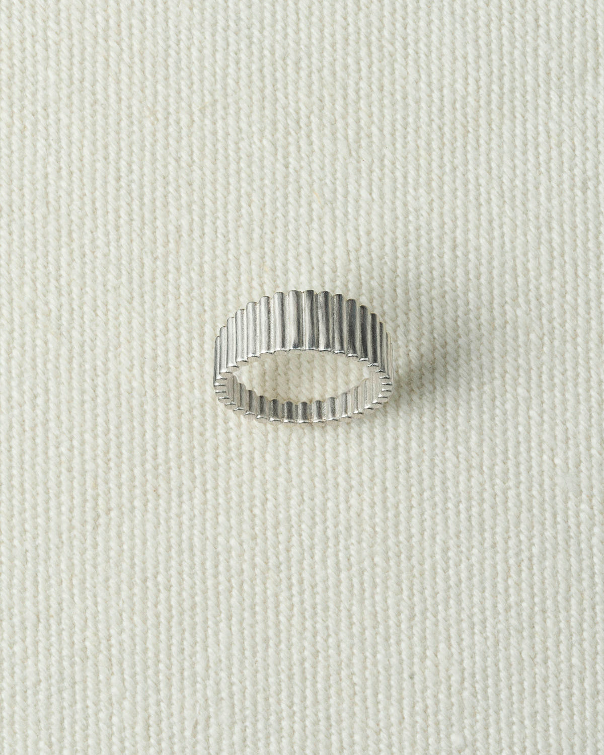 Silver ribbed band lying flat on textured ecru canvas