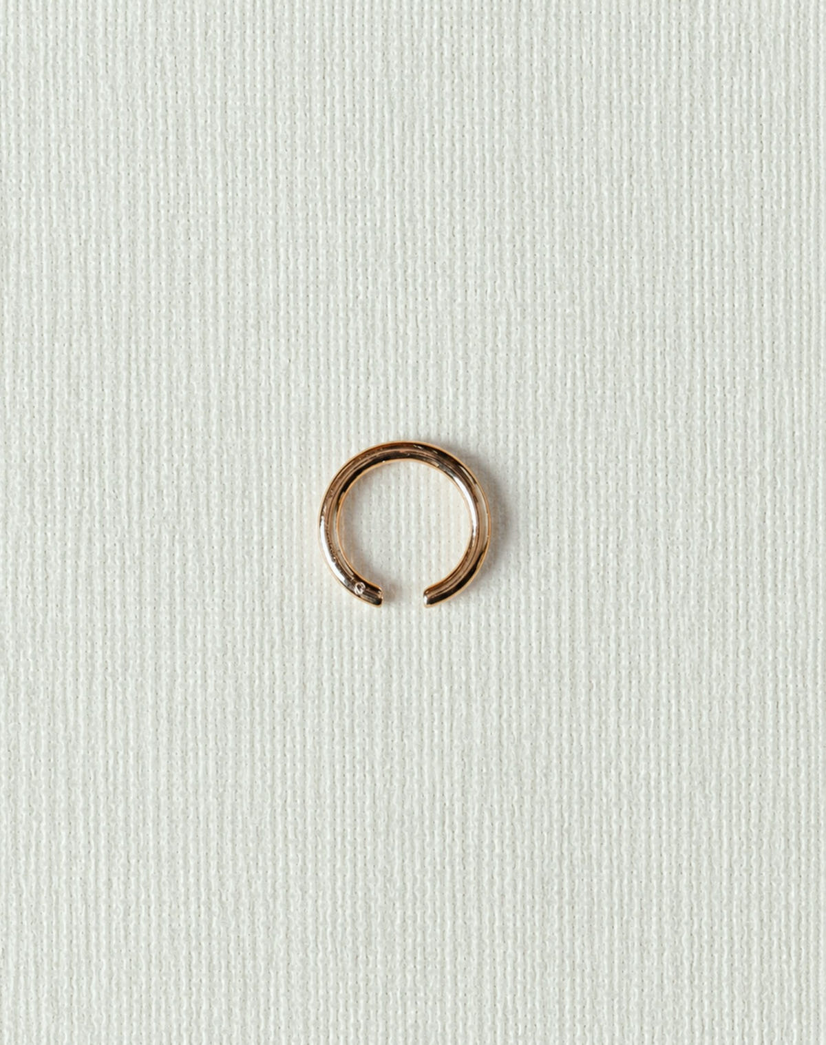 Small open gold ring with a smooth band, flat on textured paper