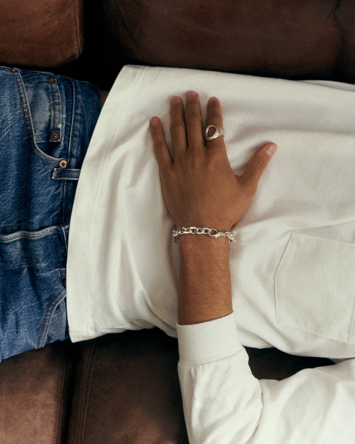 Grosse maille argentée au poignet, main posée sur un sweat blanc, bague argentée