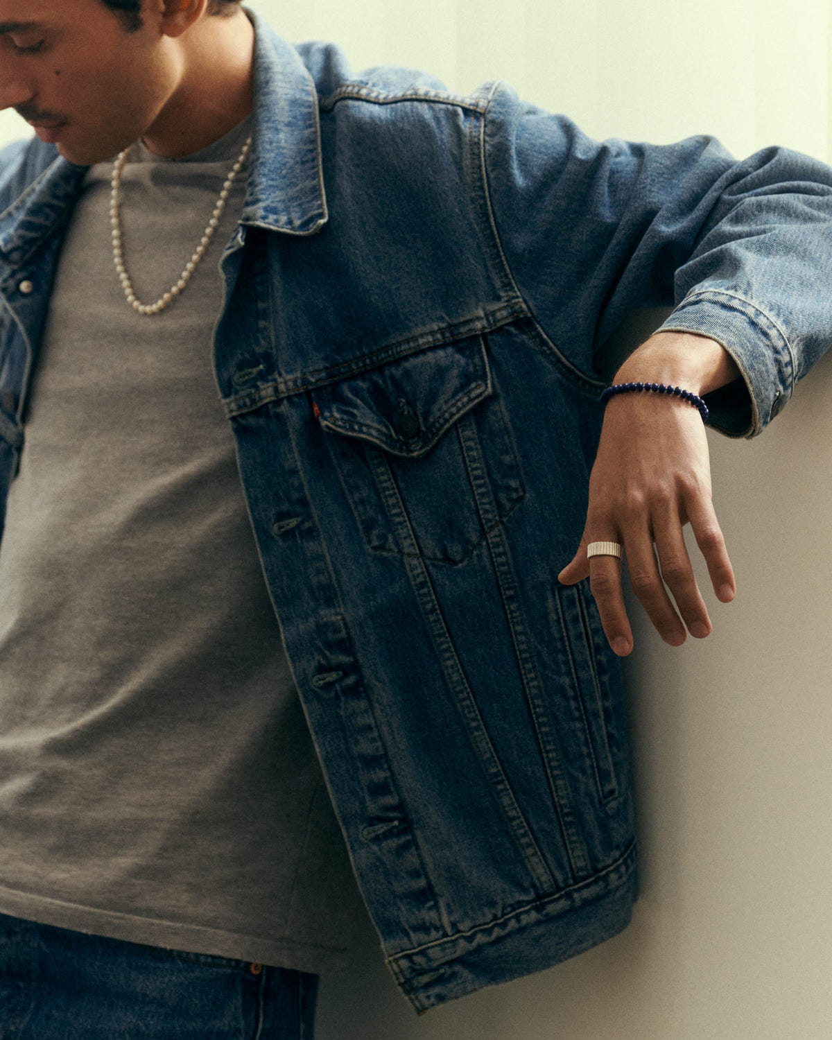 Perles bleu nuit au poignet, bras appuyé au mur, veste en jean ouverte