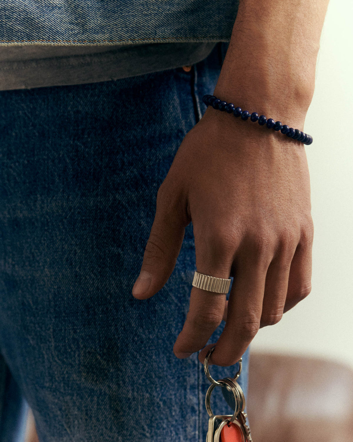 Perles bleu nuit au poignet, bague argentée striée, main le long d'un jean
