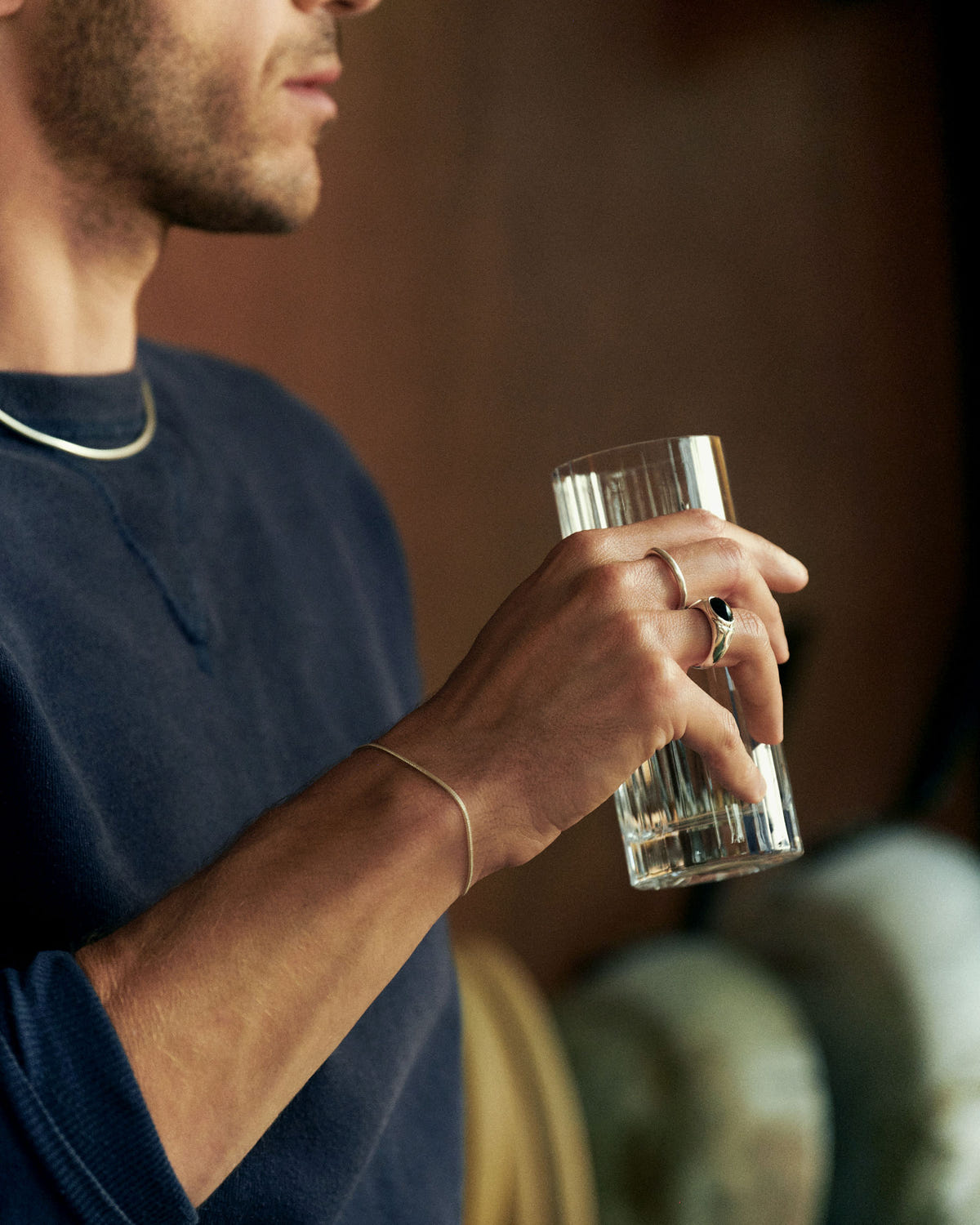 Fine gold chain at the wrist, hand holding a fluted glass, navy sweatshirt