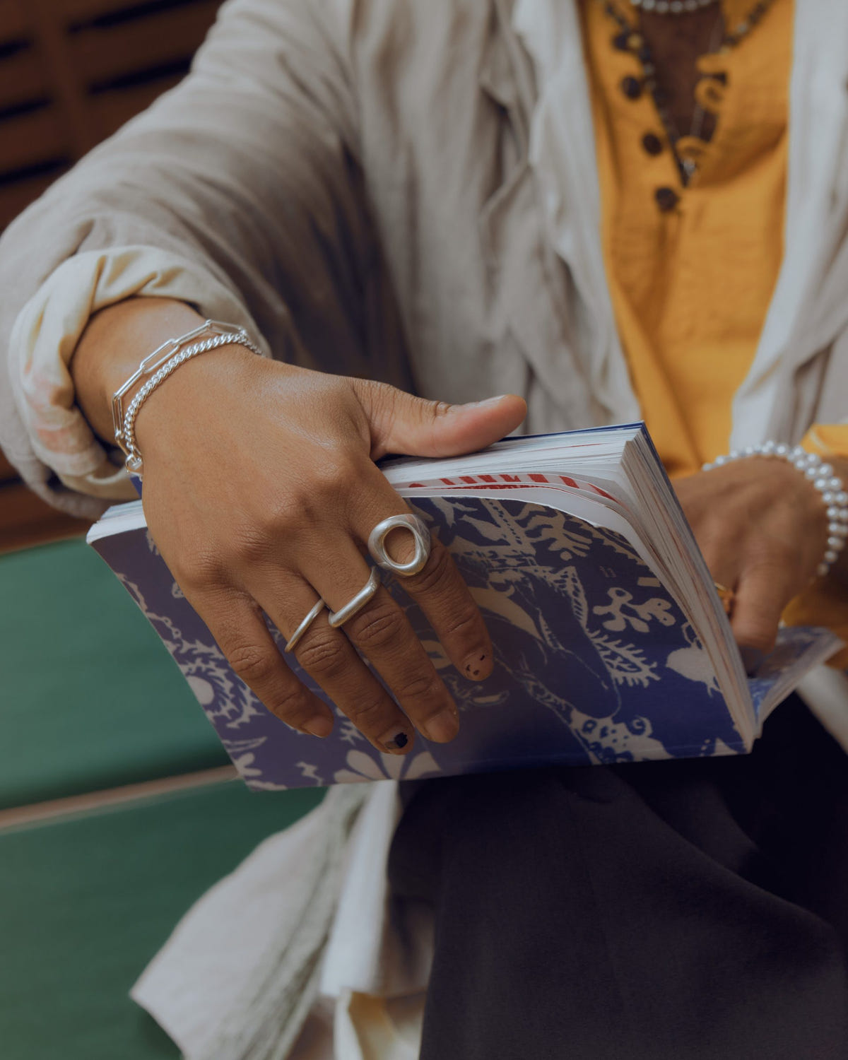 Au poignet avec des bagues argentées, mains tenant un livre à couverture bleue à motifs