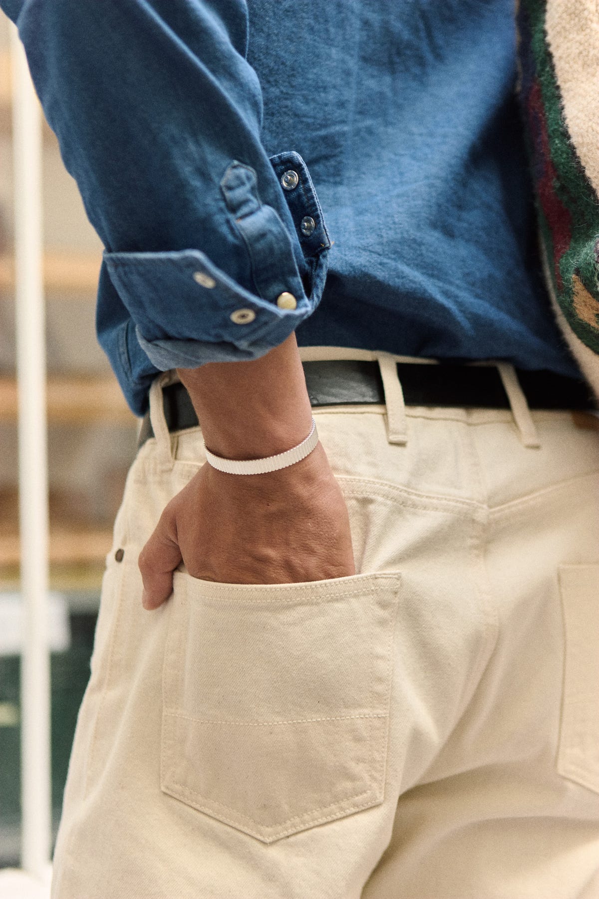 Ribbed silver cuff on the wrist, hand slipped into the back pocket of ecru jeans, denim shirt