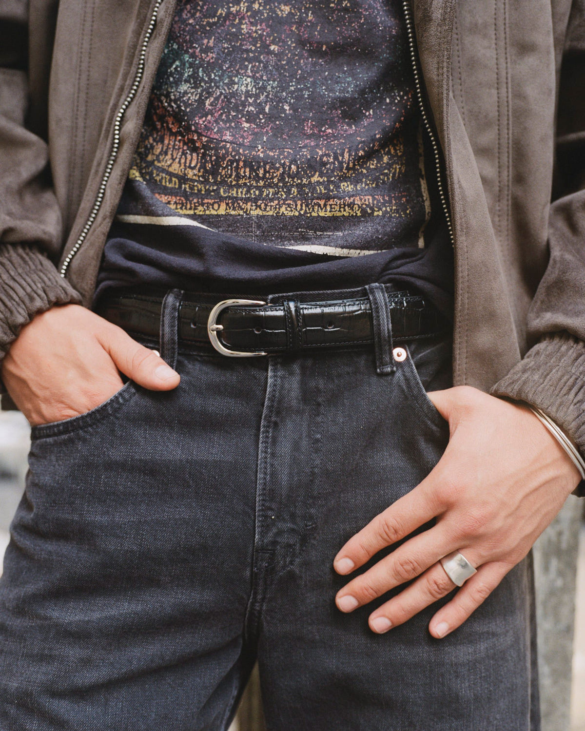 Embossed black leather belt with silver buckle on dark denim, silver flat band ring on the hand
