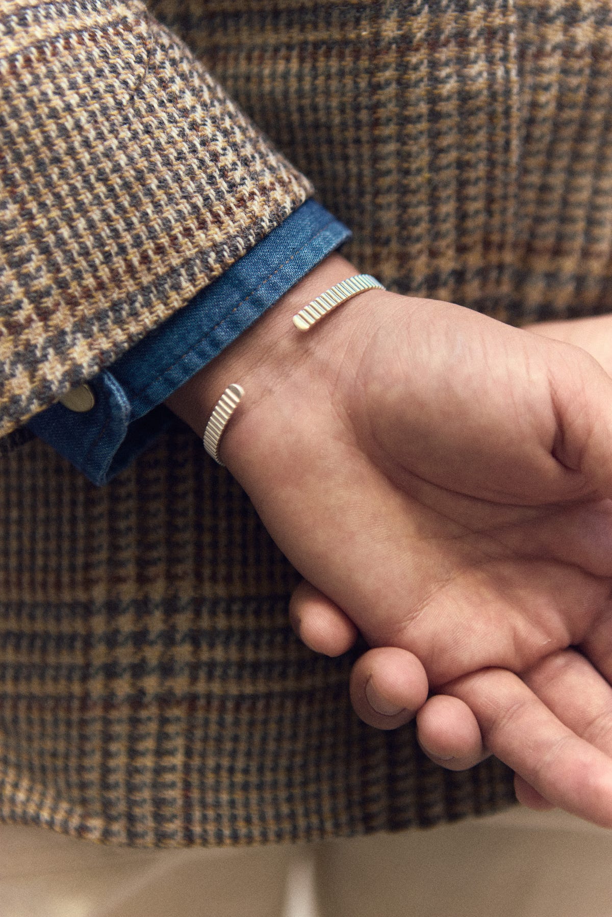 Close-up of the open ends of the silver cuff on the inner wrist, hands clasped, tweed sleeve