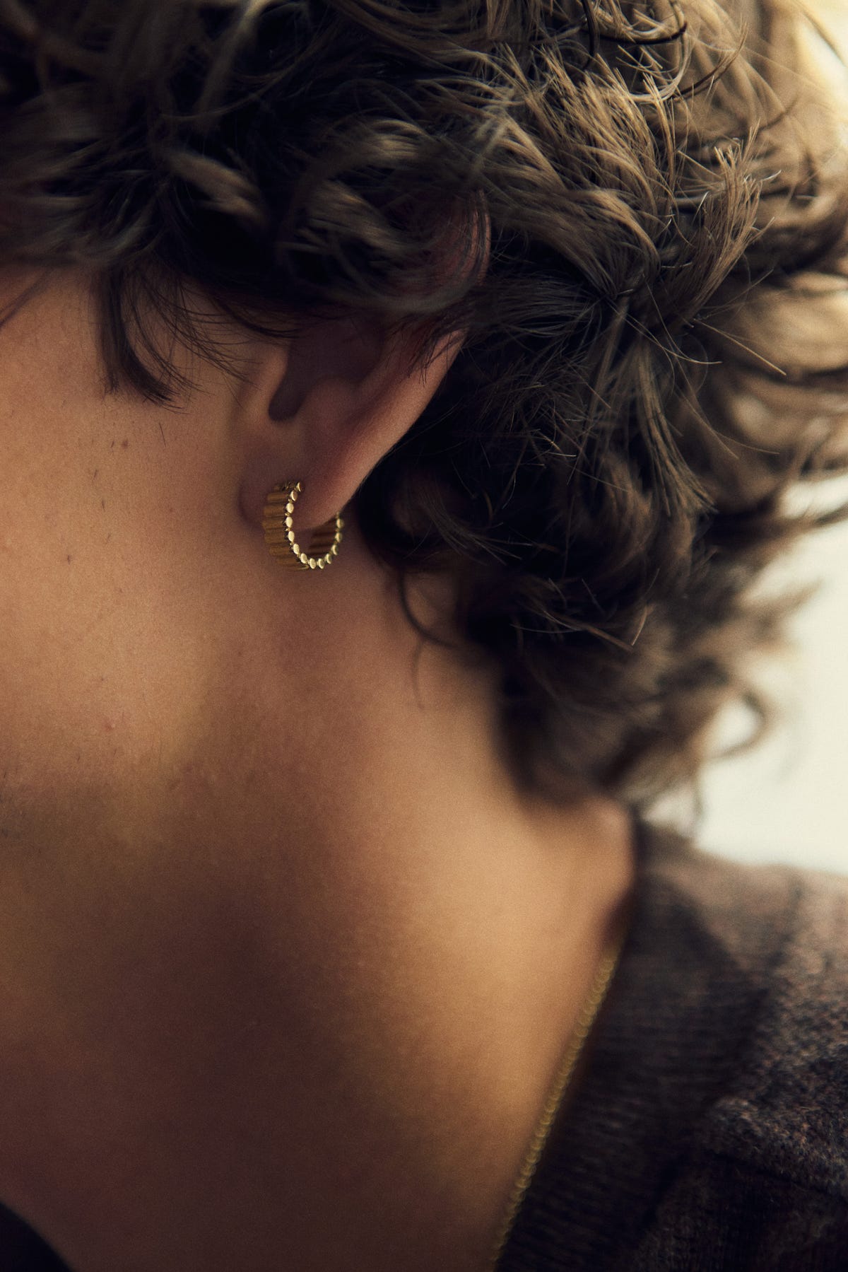 Gold hoop with ribbed segments and beaded edges on the earlobe, fine chain, brown knit collar