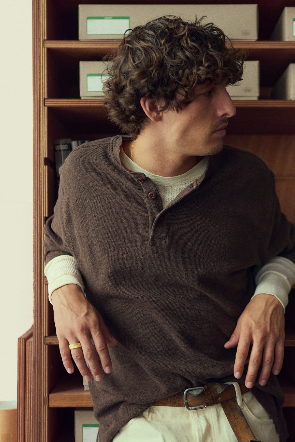Gold band worn while leaning against wooden shelves, brown henley over a cream waffle top