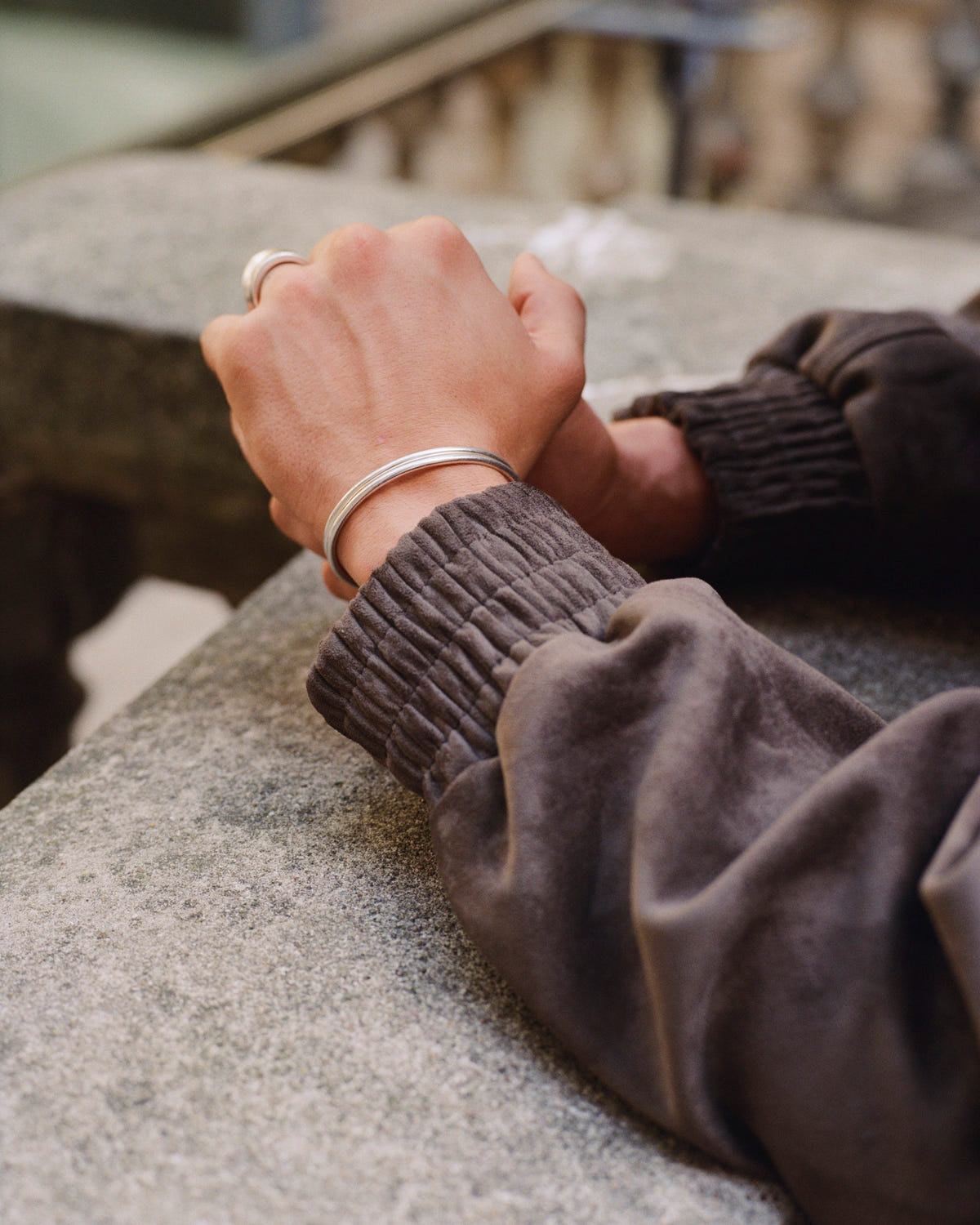 Silver-plated double cuff 3mm on the wrist, hands clasped on a stone ledge, dark sweatshirt