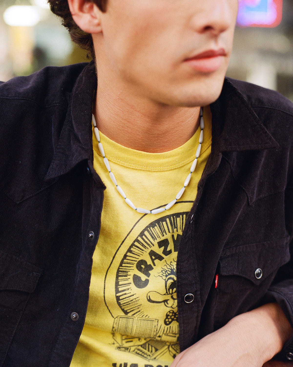 Mother-of-pearl drop bead necklace worn over a yellow printed tee, black corduroy shirt