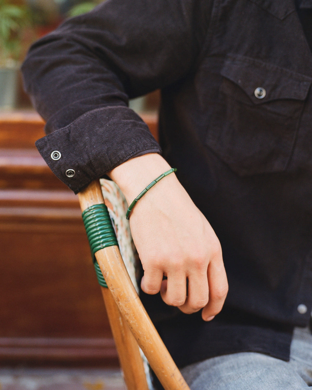 Green jade tube bead bracelet on the wrist, hand resting on a bistro chair, black shirt