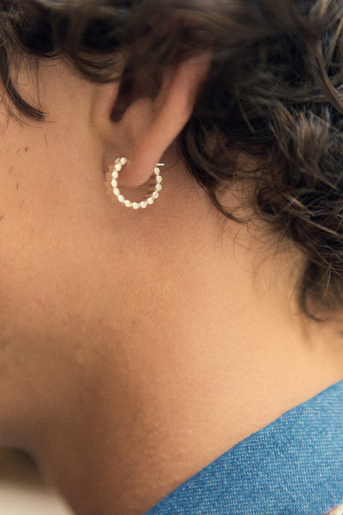 Silver hoop on the earlobe, head in profile, curly hair and denim collar