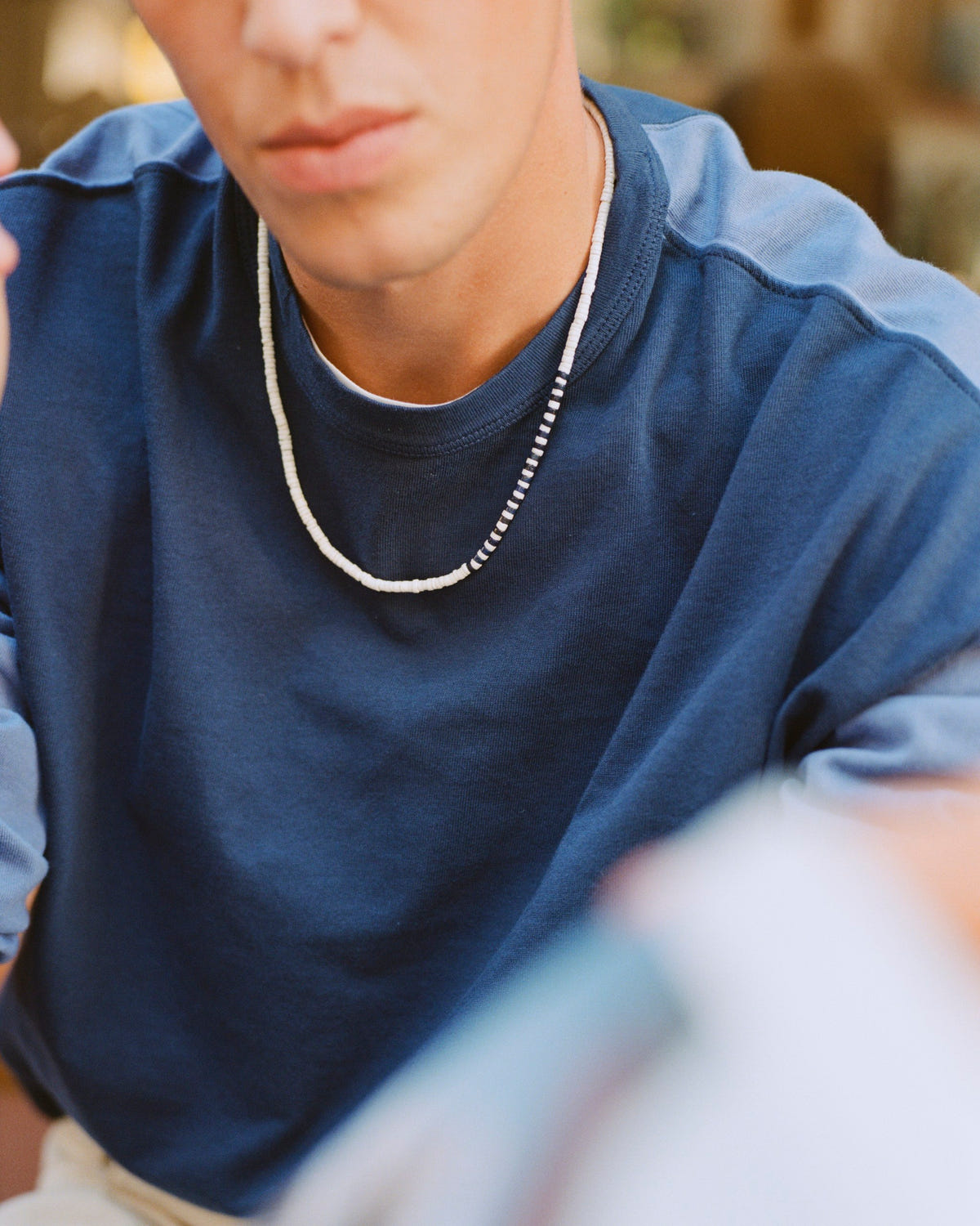 White seashell striped bead necklace worn over a two-tone blue tee
