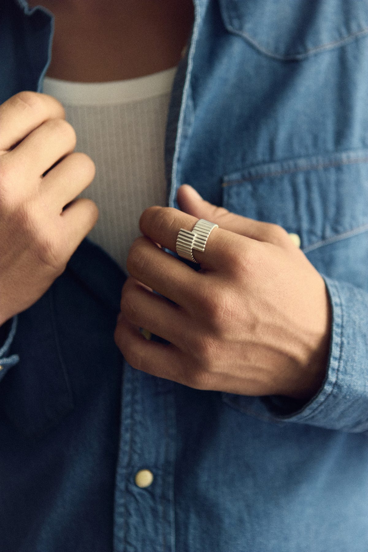 Silver ring on the index finger, hand holding an open denim shirt, white ribbed top