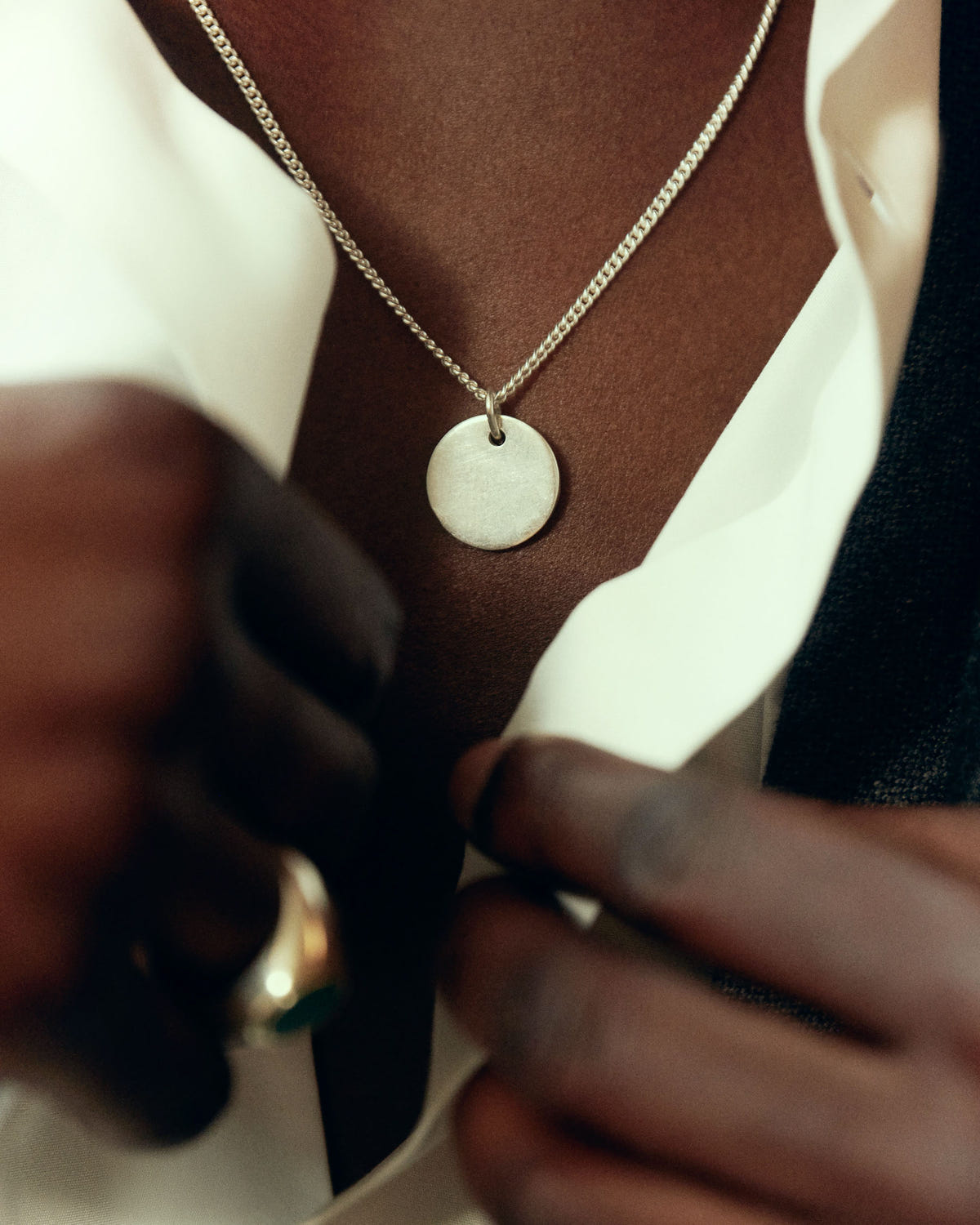 Round silver disc on a curb chain, open white shirt, close-up at the chest