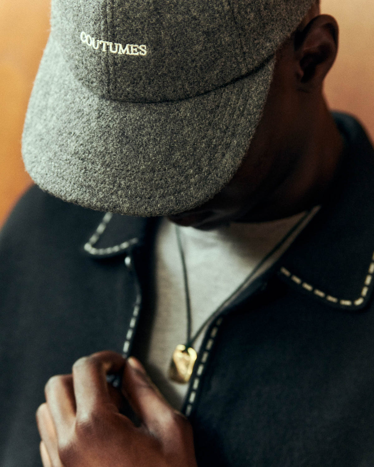 Flecked grey wool with embroidered logo, worn with a dark jacket with white stitching