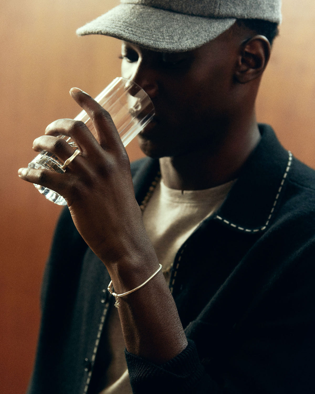 Fine gold chain on a raised wrist holding a glass, black cardigan with off-white topstitching