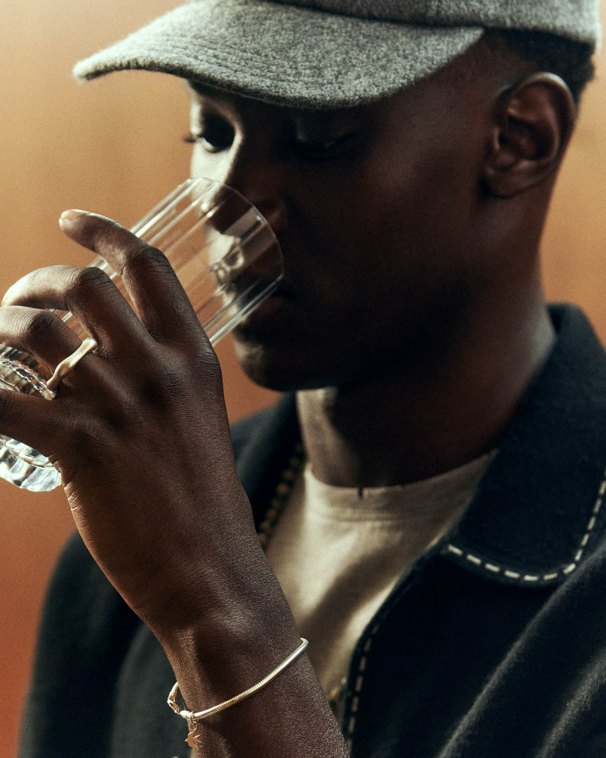 Tight crop on the grey brim, hand raising a glass, silver bangle at the wrist
