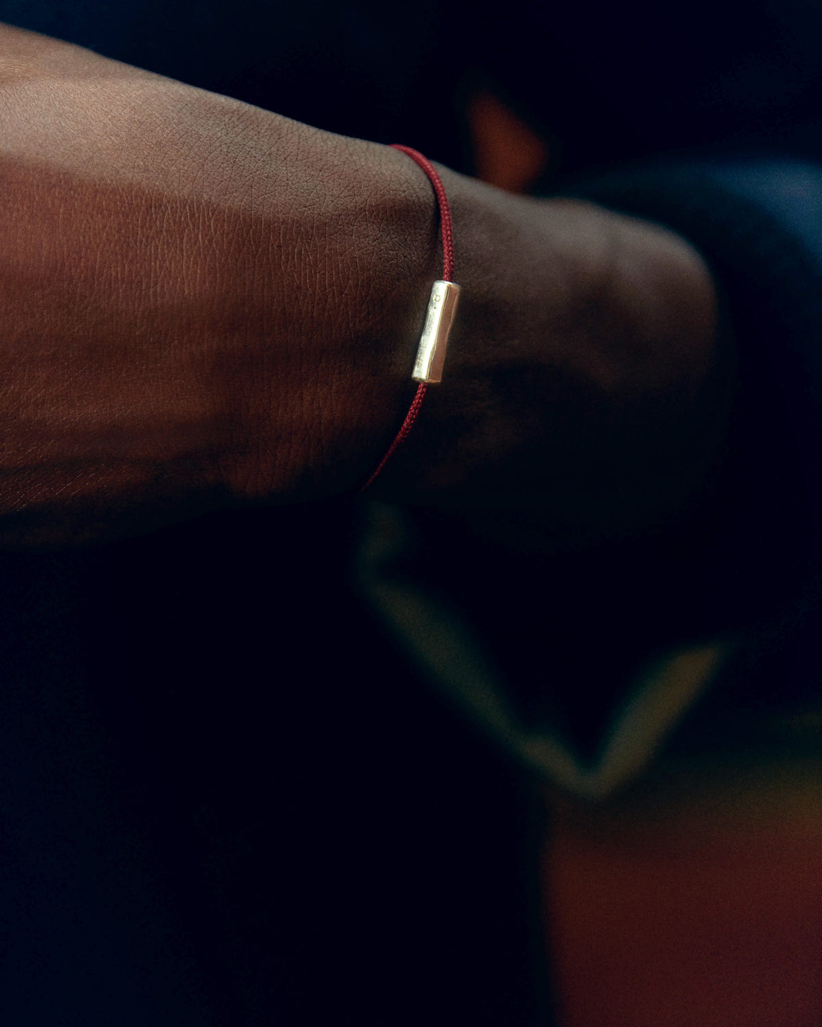 Red cord with a gold tube element, worn on the wrist in low light