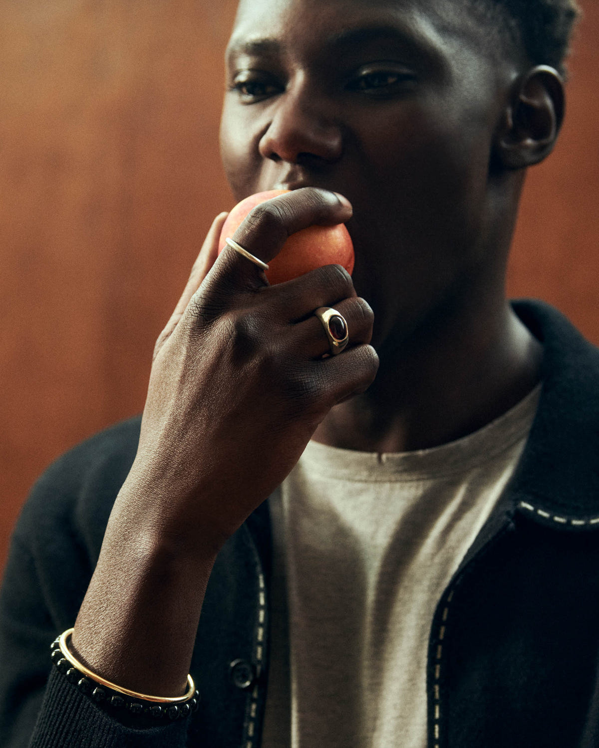 Gold with a black stone, on the hand lifting an orange fruit to the lips