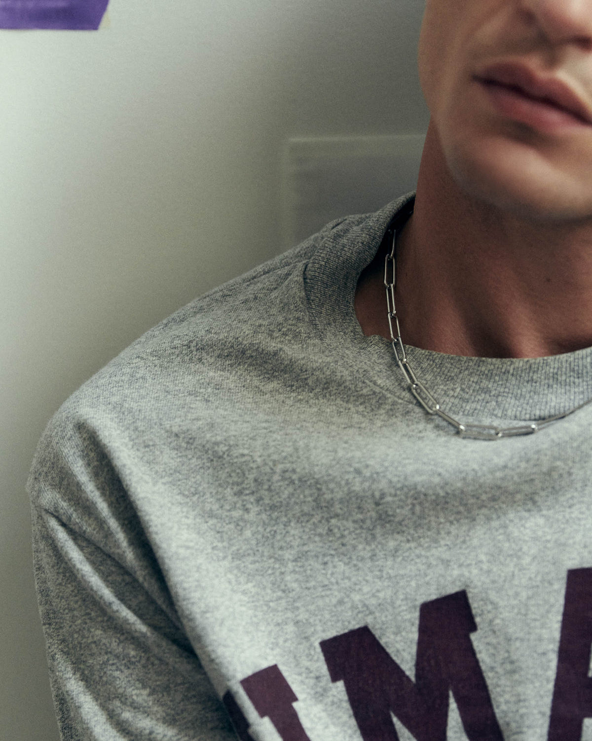 Silver elongated-link chain at the neck, marled grey sweatshirt with burgundy lettering