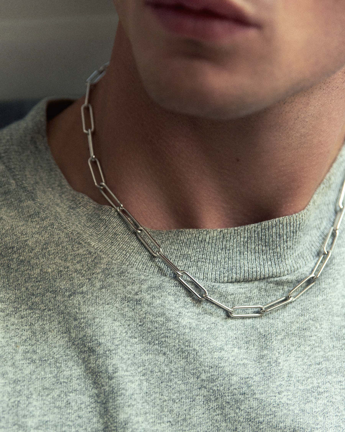 Close-up at the neck, chain worn in two lengths over a marled grey sweater