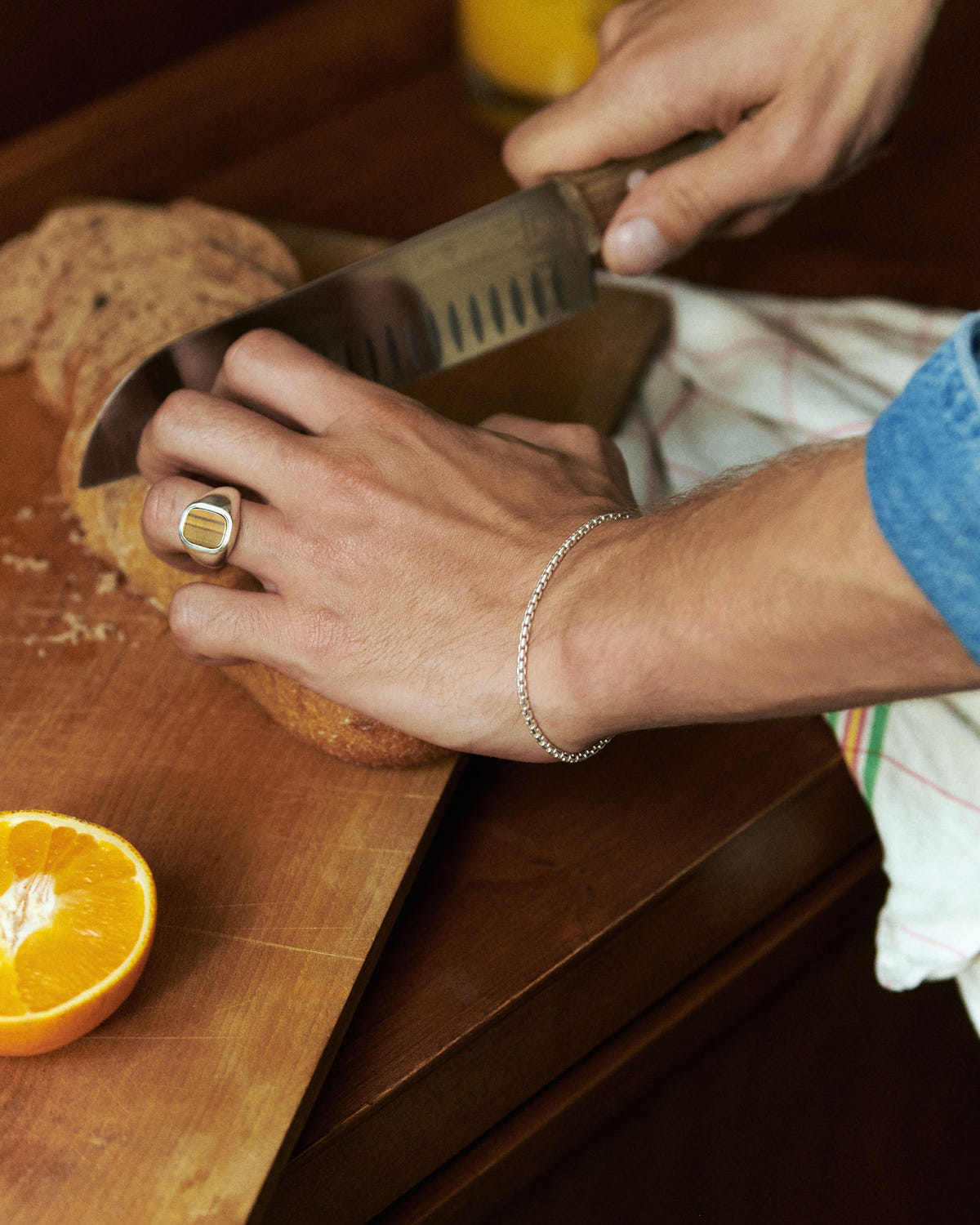 Fine chain on a wrist slicing bread, signet ring and wooden board
