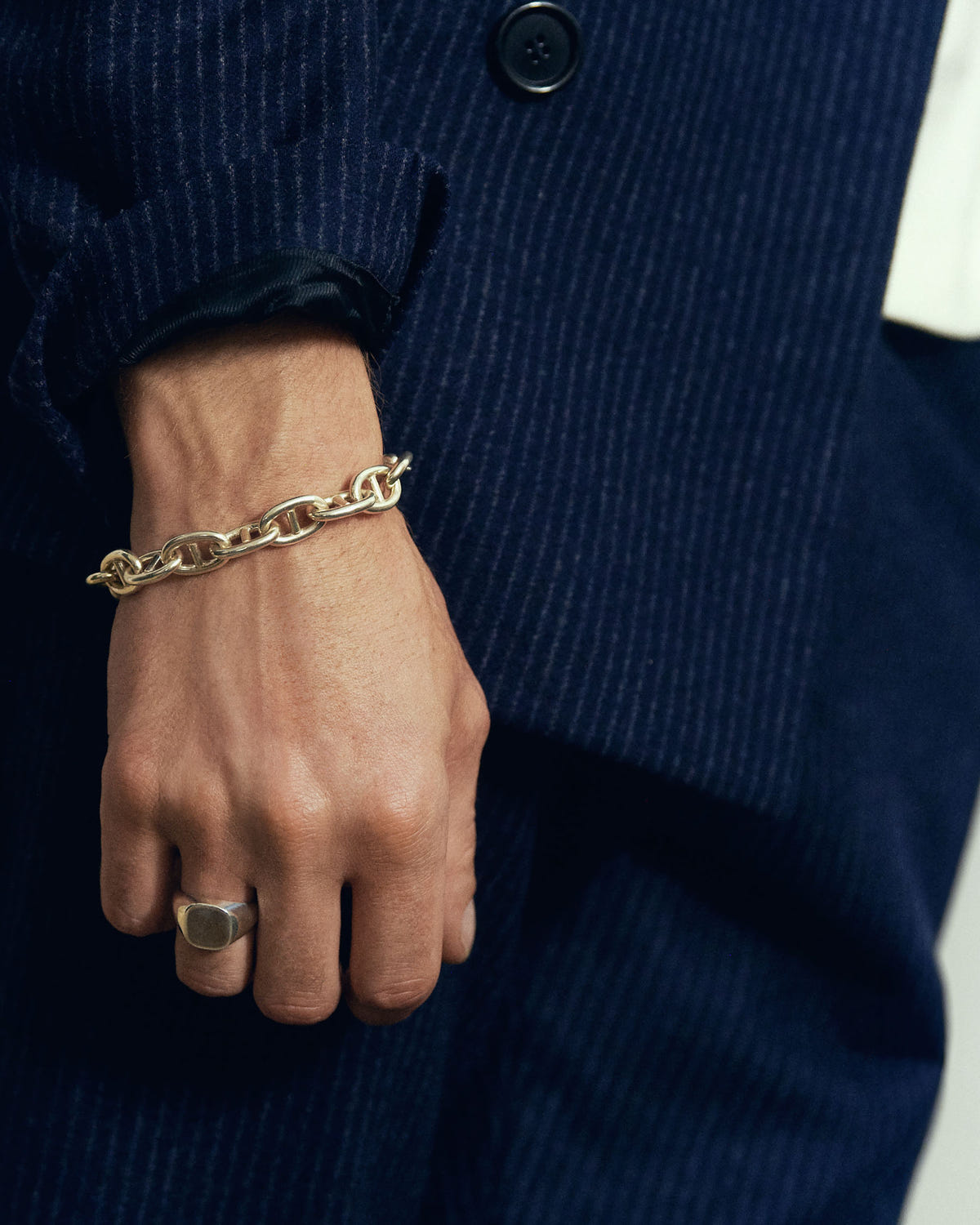 Portée à l'auriculaire avec un bracelet à maillons argenté, sur veste marine rayée