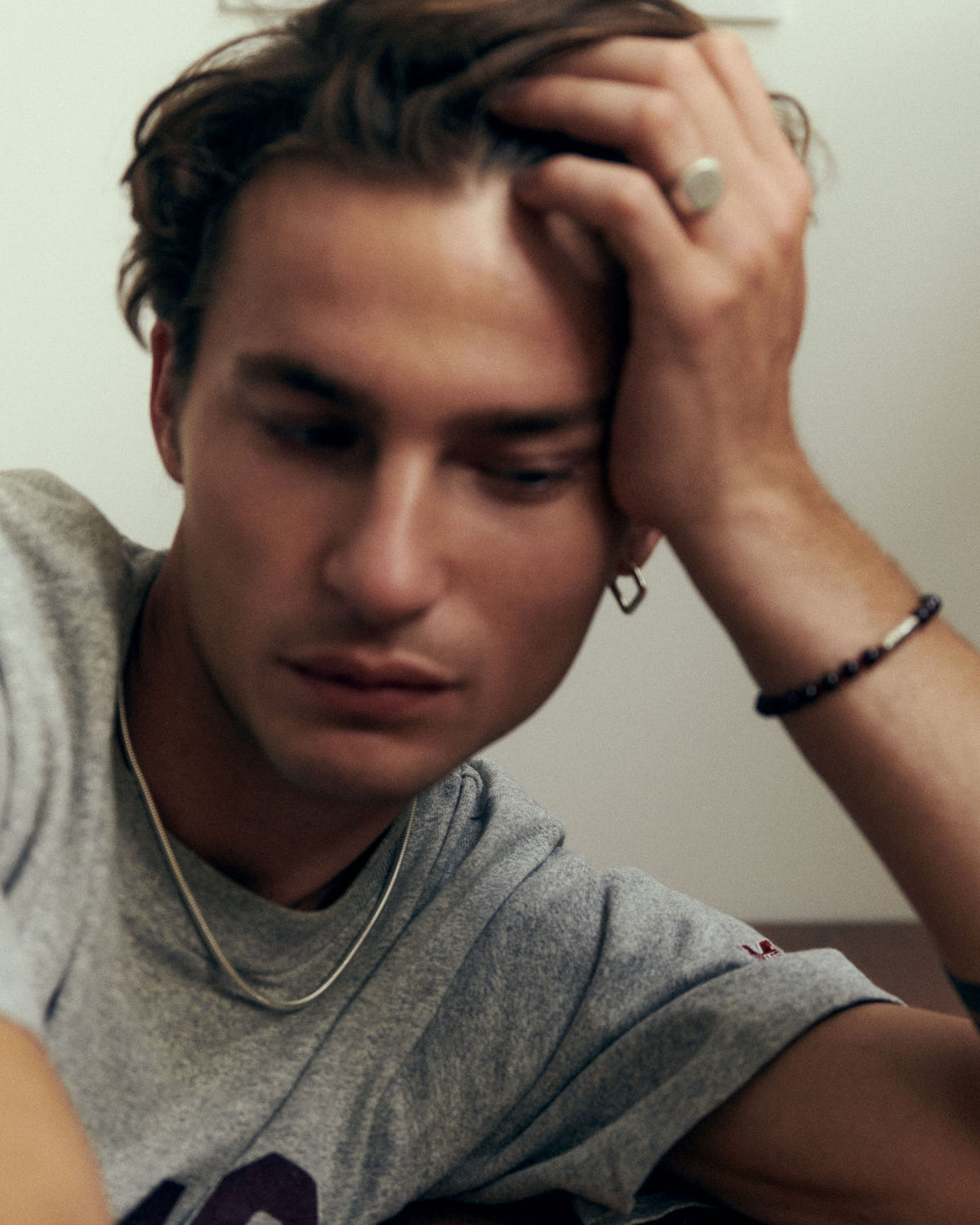 Fine chain falling over a heather grey tee, head resting on the hand