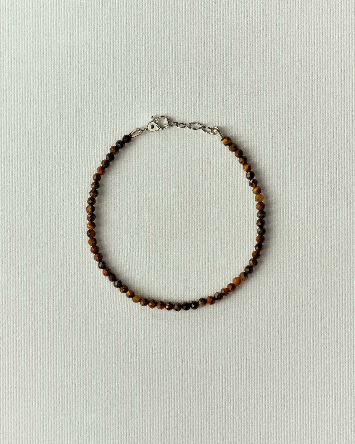 Minuscules perles facettées brun ambré et fermoir argenté, en cercle sur papier écru